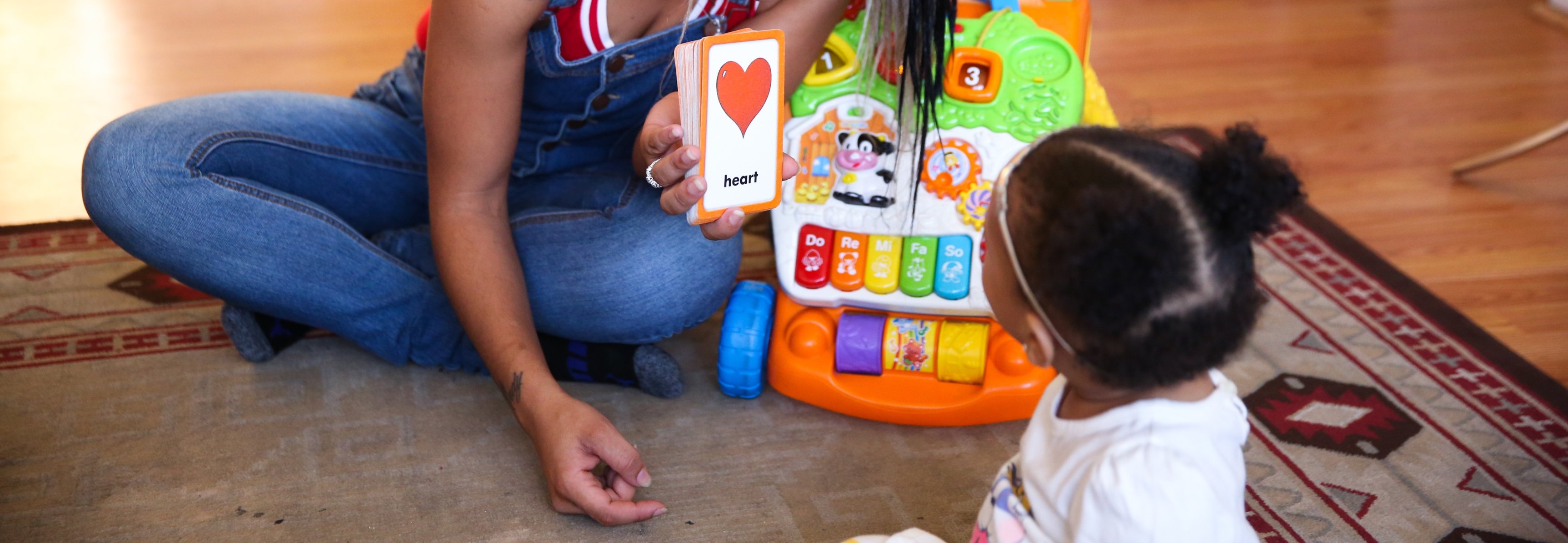 Primer plano de una madre de color mostrándole a su bebé una tarjeta con la palabra corazón escrita