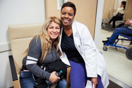 Black female nurse sitting side by side with female patient smiling