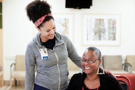 Young Black female nurse smiling down at seated Black female patient